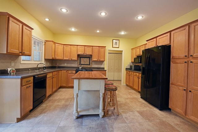 kitchen with a center island, sink, a kitchen breakfast bar, butcher block countertops, and black appliances