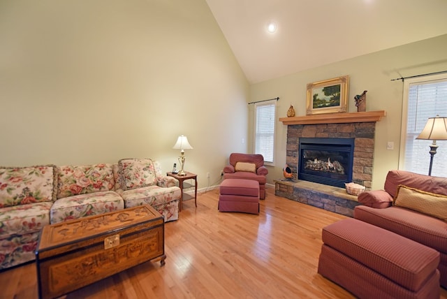 living room featuring wood-type flooring, high vaulted ceiling, and a stone fireplace