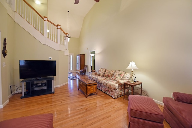 living room with ceiling fan, light hardwood / wood-style flooring, and a towering ceiling