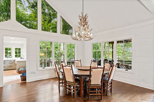 dining area featuring high vaulted ceiling, dark wood-style floors, wooden walls, an inviting chandelier, and baseboards