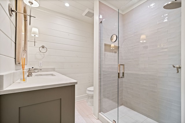 bathroom with vanity, wooden walls, toilet, and a tile shower