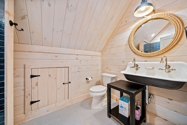 bathroom featuring toilet, a sink, wooden walls, wood ceiling, and vaulted ceiling