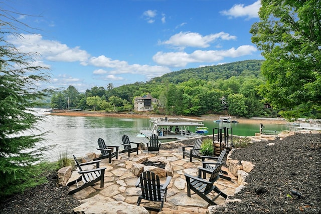 view of patio / terrace featuring a wooded view, a dock, a water view, and an outdoor fire pit