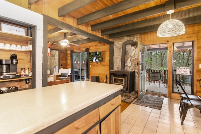 kitchen with pendant lighting, wooden walls, a wood stove, wood ceiling, and beam ceiling