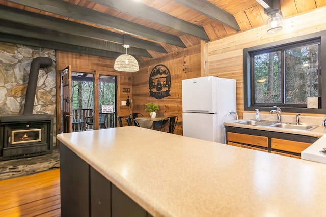 kitchen with sink, hanging light fixtures, wooden walls, wooden ceiling, and white fridge