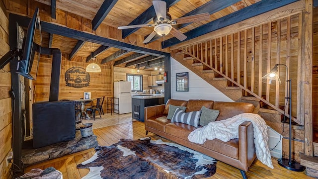 living room with wood ceiling, wooden walls, light hardwood / wood-style floors, beamed ceiling, and a wood stove