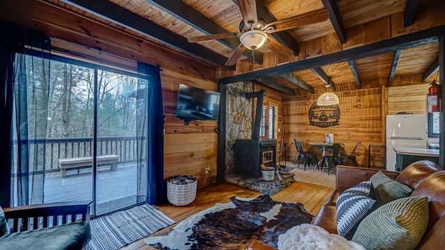 living room with hardwood / wood-style floors, wood walls, beamed ceiling, a wood stove, and ceiling fan