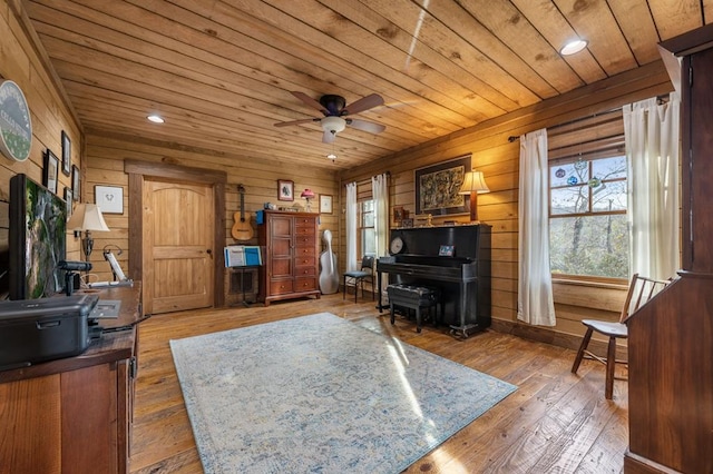 sitting room with light wood-type flooring, wood ceiling, ceiling fan, and wood walls