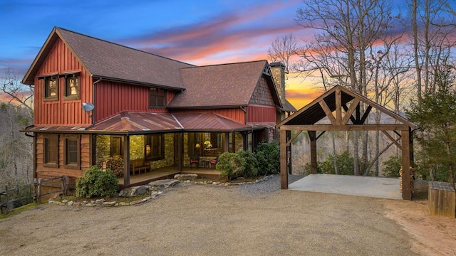 back of house at dusk with fence, a shingled roof, a porch, a chimney, and driveway