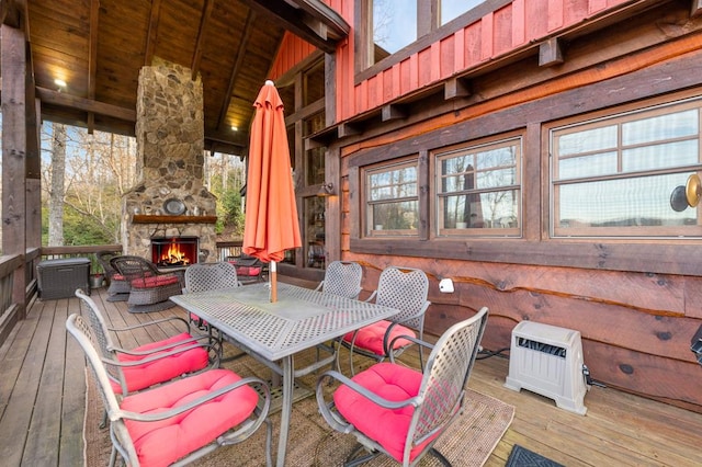 deck featuring outdoor dining space, heating unit, and an outdoor stone fireplace