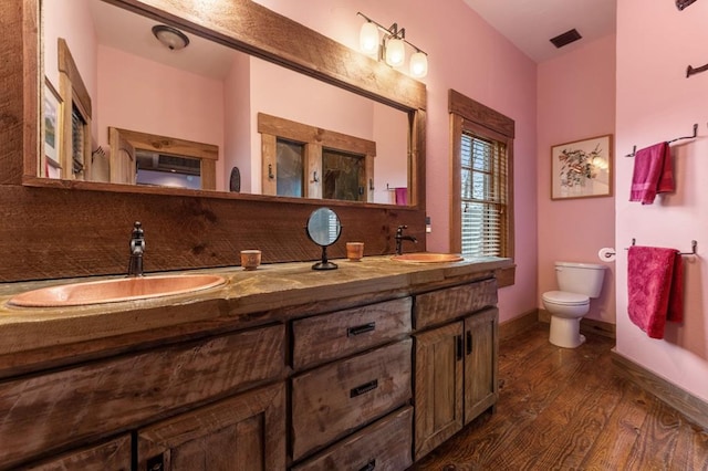 bathroom featuring double vanity, toilet, a sink, and wood finished floors