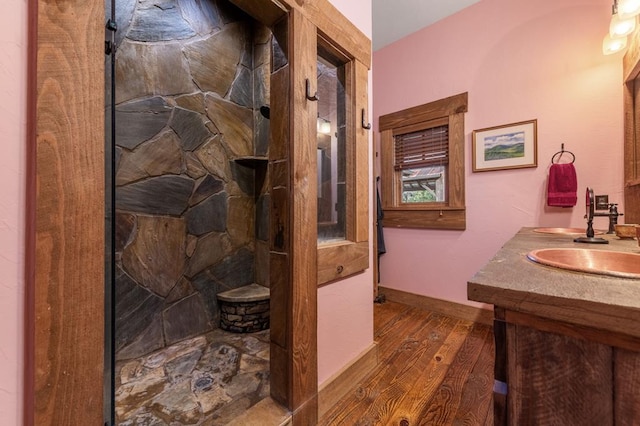 bathroom with double vanity, wood finished floors, baseboards, walk in shower, and a sink