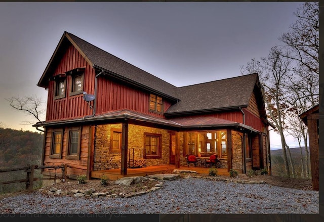 rear view of property featuring a shingled roof, fence, covered porch, and stone siding