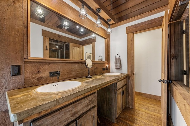 bathroom featuring baseboards, a sink, wood finished floors, and double vanity