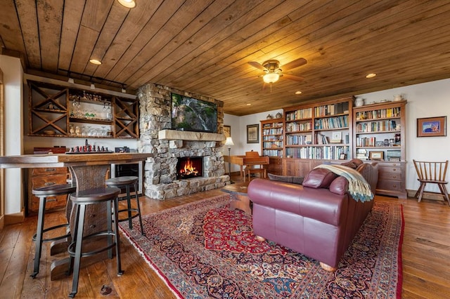 sitting room with hardwood / wood-style floors, a stone fireplace, recessed lighting, wood ceiling, and a bar
