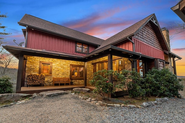 view of front of property featuring covered porch, stone siding, a chimney, a shingled roof, and board and batten siding
