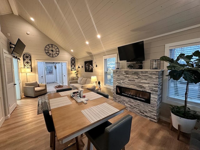 dining room featuring wood walls, wood ceiling, high vaulted ceiling, light hardwood / wood-style flooring, and a fireplace