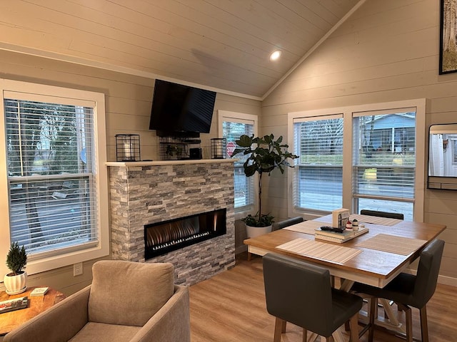 dining room with lofted ceiling, a stone fireplace, wood walls, and light wood-type flooring