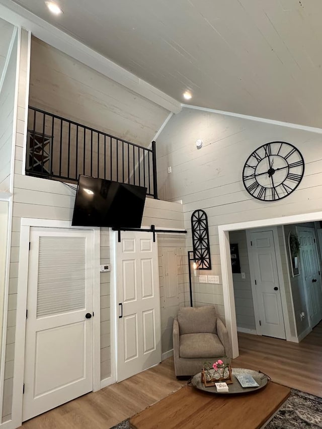 living area with wooden walls, a barn door, lofted ceiling with beams, and hardwood / wood-style floors