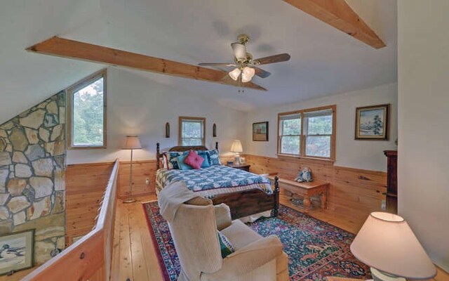 living room featuring wooden walls, ceiling fan, a stone fireplace, and high vaulted ceiling