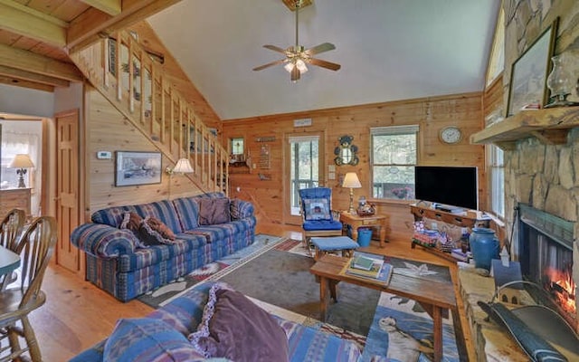 living room featuring wooden walls, a fireplace, light wood-type flooring, ceiling fan, and beam ceiling