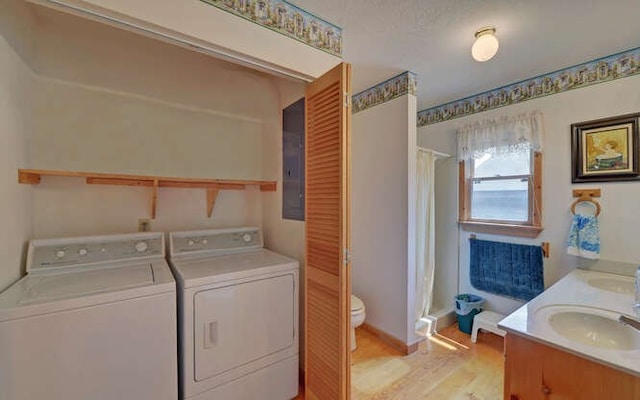 laundry room featuring washer and dryer, sink, electric panel, and light hardwood / wood-style flooring