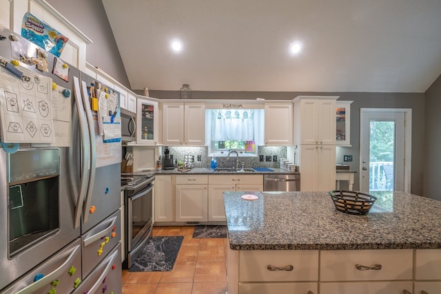 kitchen featuring tasteful backsplash, dark stone counters, lofted ceiling, appliances with stainless steel finishes, and a sink