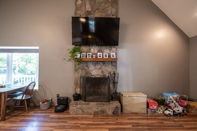 living area with a stone fireplace, wood finished floors, and high vaulted ceiling