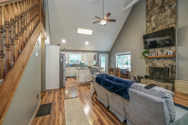 living area featuring light wood-type flooring, visible vents, high vaulted ceiling, a fireplace, and stairs