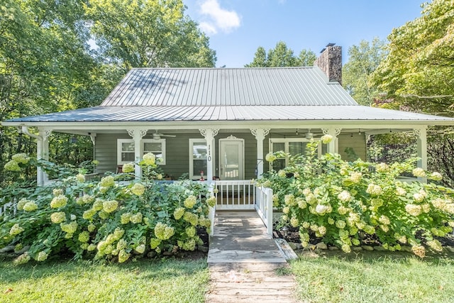 farmhouse featuring ceiling fan, a porch, metal roof, and a chimney