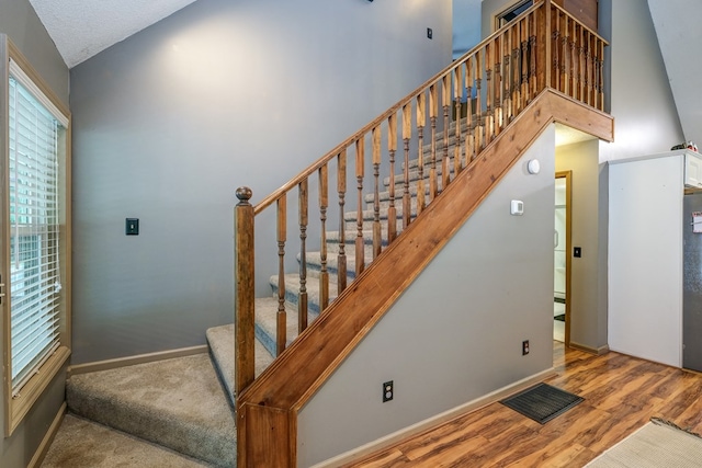 staircase with visible vents, baseboards, high vaulted ceiling, and wood finished floors