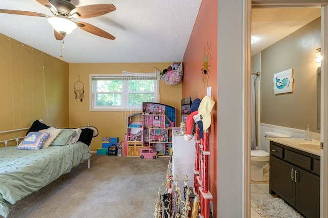 bedroom with ceiling fan, a wainscoted wall, light colored carpet, a textured ceiling, and a sink