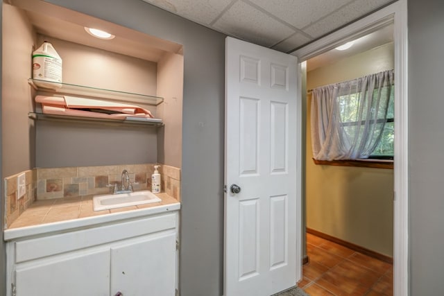 bathroom with a drop ceiling, baseboards, and vanity