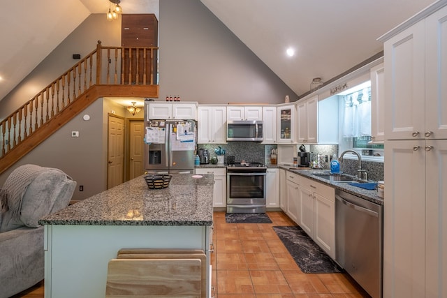 kitchen featuring tasteful backsplash, dark stone countertops, white cabinets, stainless steel appliances, and a sink