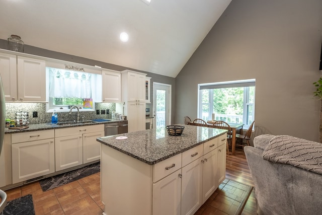 kitchen with a kitchen island, dark stone counters, a sink, decorative backsplash, and dishwasher