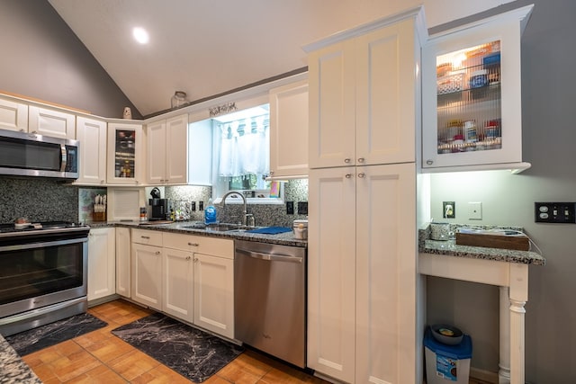 kitchen featuring dark stone counters, lofted ceiling, decorative backsplash, appliances with stainless steel finishes, and a sink