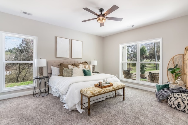 carpeted bedroom featuring visible vents, multiple windows, baseboards, and a ceiling fan