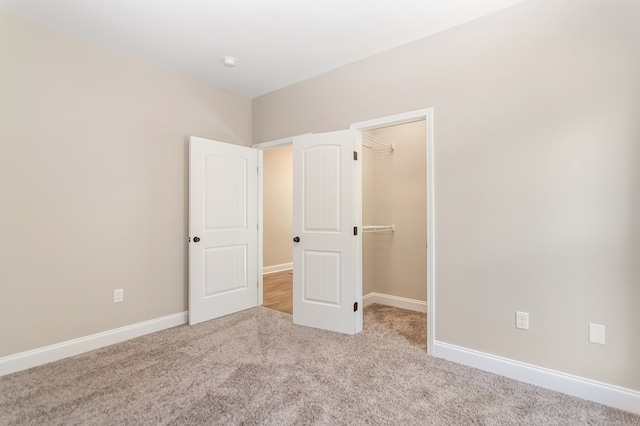 unfurnished bedroom featuring a walk in closet, carpet, baseboards, and a closet