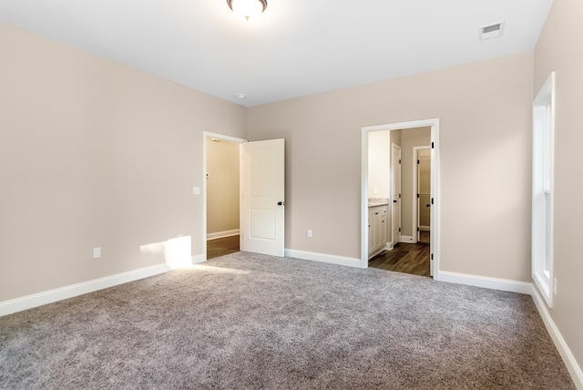 unfurnished bedroom with dark carpet, ensuite bathroom, and baseboards