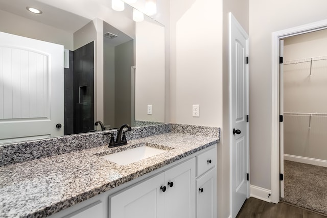 bathroom featuring vanity, wood finished floors, visible vents, baseboards, and a walk in closet