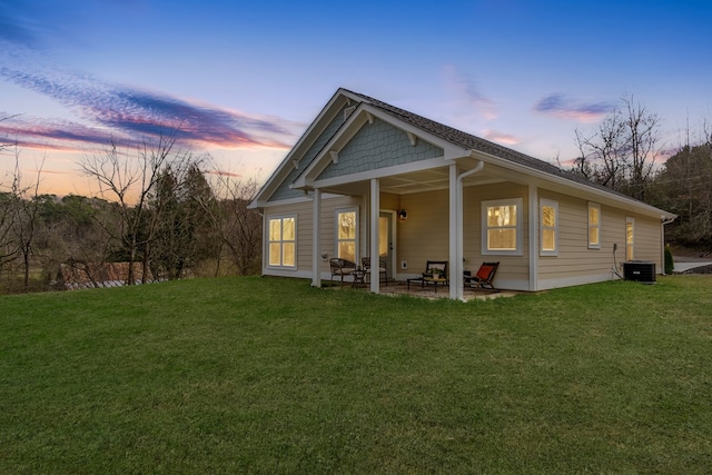 back of house at dusk with a lawn, cooling unit, and a patio