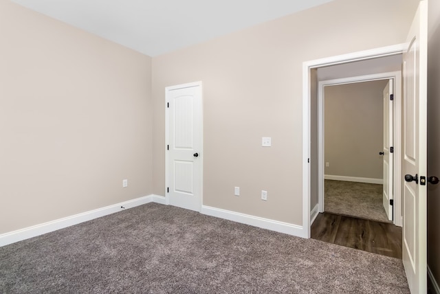 unfurnished bedroom with dark carpet and baseboards