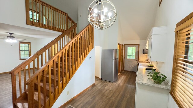 staircase featuring hardwood / wood-style flooring, ceiling fan with notable chandelier, a high ceiling, and a healthy amount of sunlight