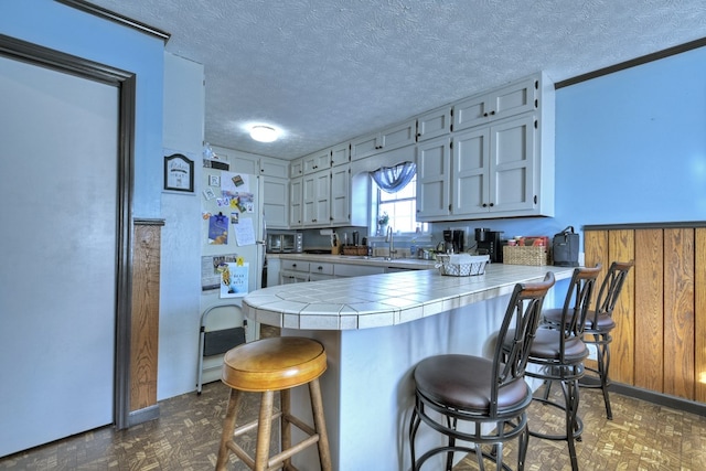 kitchen featuring a breakfast bar, sink, tile counters, kitchen peninsula, and a textured ceiling