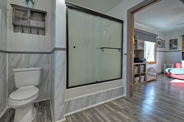 bathroom with hardwood / wood-style floors, combined bath / shower with glass door, and toilet