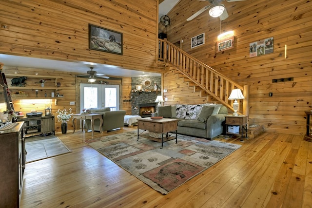 living room with a fireplace, a high ceiling, light hardwood / wood-style flooring, and wooden walls