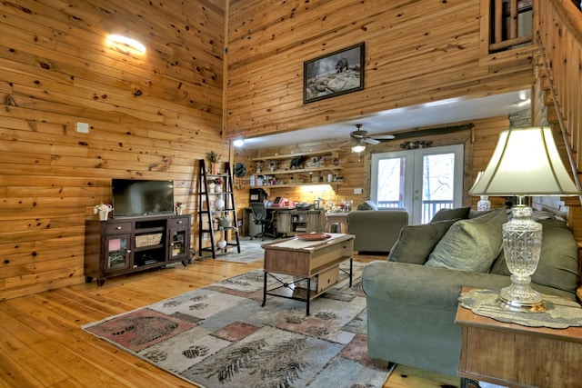 living room featuring hardwood / wood-style floors, wood walls, a high ceiling, and french doors