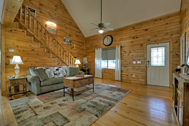 living room featuring ceiling fan, light hardwood / wood-style flooring, high vaulted ceiling, and wooden walls