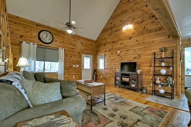 living room featuring light wood-type flooring, high vaulted ceiling, ceiling fan, and wood walls