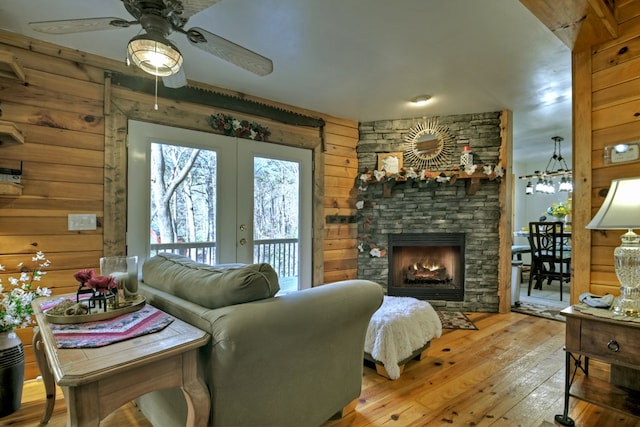 living room featuring ceiling fan, french doors, light hardwood / wood-style floors, wooden walls, and a fireplace